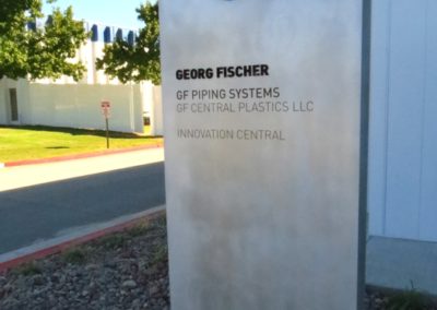 Picture of metal monolith type sign in front of building, silver with blue letters.