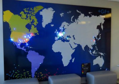 Photo of a large map of the world with different colored LED pin lights in various areas.