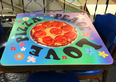 A colorful picture of another table top that says Peace, Love, Pizza!