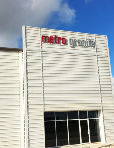 Picture of red and silver metal letters at the top of a building wall that says Metro Granite.