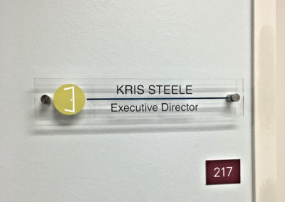 Picture of a clear name plate with metal wall standoffs.
